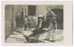 Item 30. Eisenstein pushing a woman (unidentified) in a wheelbarrow in the Hacienda courtyard. Several saddled horses in background.