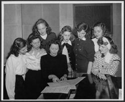 Eight unidentified women around piano looking at music manuscript.