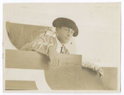 Item 0122. Two similar medium shots of Liceaga standing behind the barrier at the bullring. His arms are resting on top of the barrier, a cape is stretched out on the empty seats behind him. His head is turned slightly toward the camera.