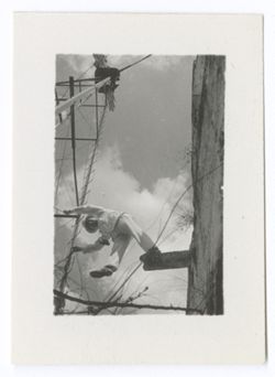 Item 1208. - 1208a. Two similar shots of unidentified man standing on a board which juts out from a wall on the right. He is leaning forward toward a windmill on the left. Taken from below.