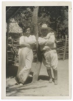 Item 0475. Eisenstein leaning against a pole supporting an overhang. Leaning against opposite side of pole, a heavy-set man wearing knee boots, a holster with pistol and a flat-brimmed hat. Possibly taken in or near Tehuantepec.