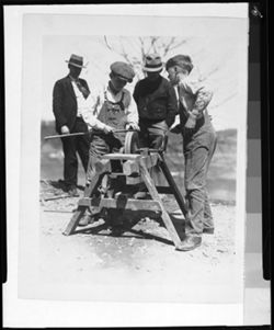 Two men and two boys using grindstone