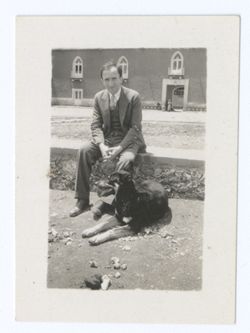 Item 1147. Julio Saldivar seated on low stone wall in courtyard of Hacienda, with dog lying at his feet.