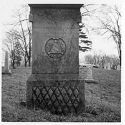 Tassled Pillow on monument. Fraternal [drawing of a triangle (with dots at each corner of the triangle) within a circle with the letters K, L, of H surrounding each side]