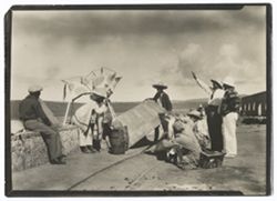Item 0388. Filming scene with "Sebastian" (Martin Hernandez) and Corpus Christi bull. From left, unidentified man holding reflector; "Sebastian" crouching beneath bull; unidentified man with reflector; Tissé seated on ground, filming; Alexandrov, kneeling to his right; Agustin Leiva (arm raised) standing behind Alexandrov; Eisenstein standing beside Leiva.