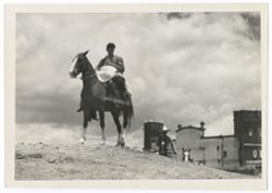 Item 0223. Hacienda owner (Julio Saldivar) on horseback on top of a hill with the body of his "daughter" lying over the saddle in front of him. Just visible over the edge of the hill behind him and to the right is another rider leading a third horse. The Hacienda in the background.