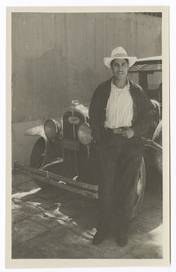 Item 0578. Unidentified man in work clothes standing beside car.