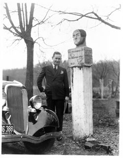 Man beside auto standing near stone head marker, Fairfax