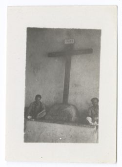 Item 1205. - 1206. Alexandrov and Eisenstein seated on either side of a large cross which stands on a rock and leans against a wall.