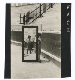Item 0985. Unidentified man holding full-length mirror in which Alexandrov is reflected as he takes this picture.